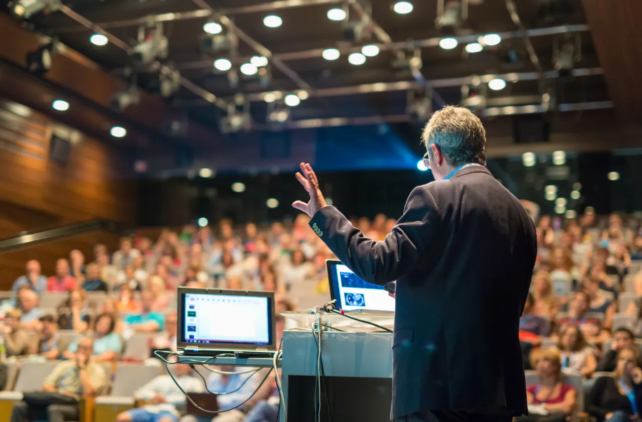 Keynote speaker addressing a large audience at a conference venue featuring event catering by Peter Rowland.