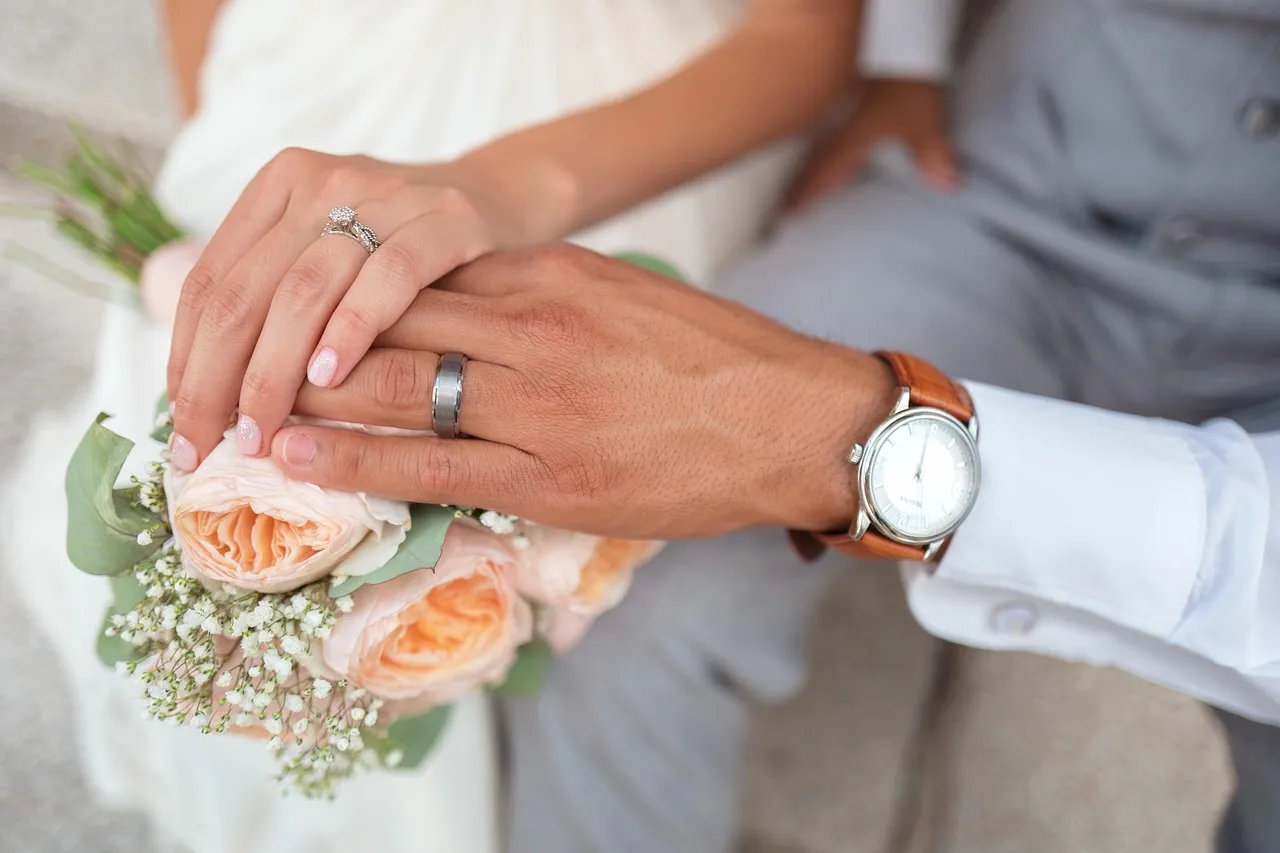 Close-up of bride and groom holding hands showing wedding rings resting on a bridal bouquet at a Peter Rowland catered wedding.