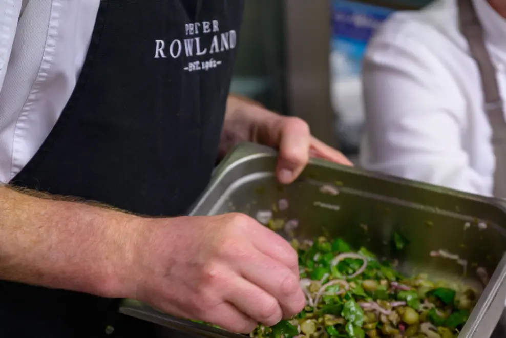 Peter Rowland chef preparing fresh ingredients in a stainless steel container for event catering.